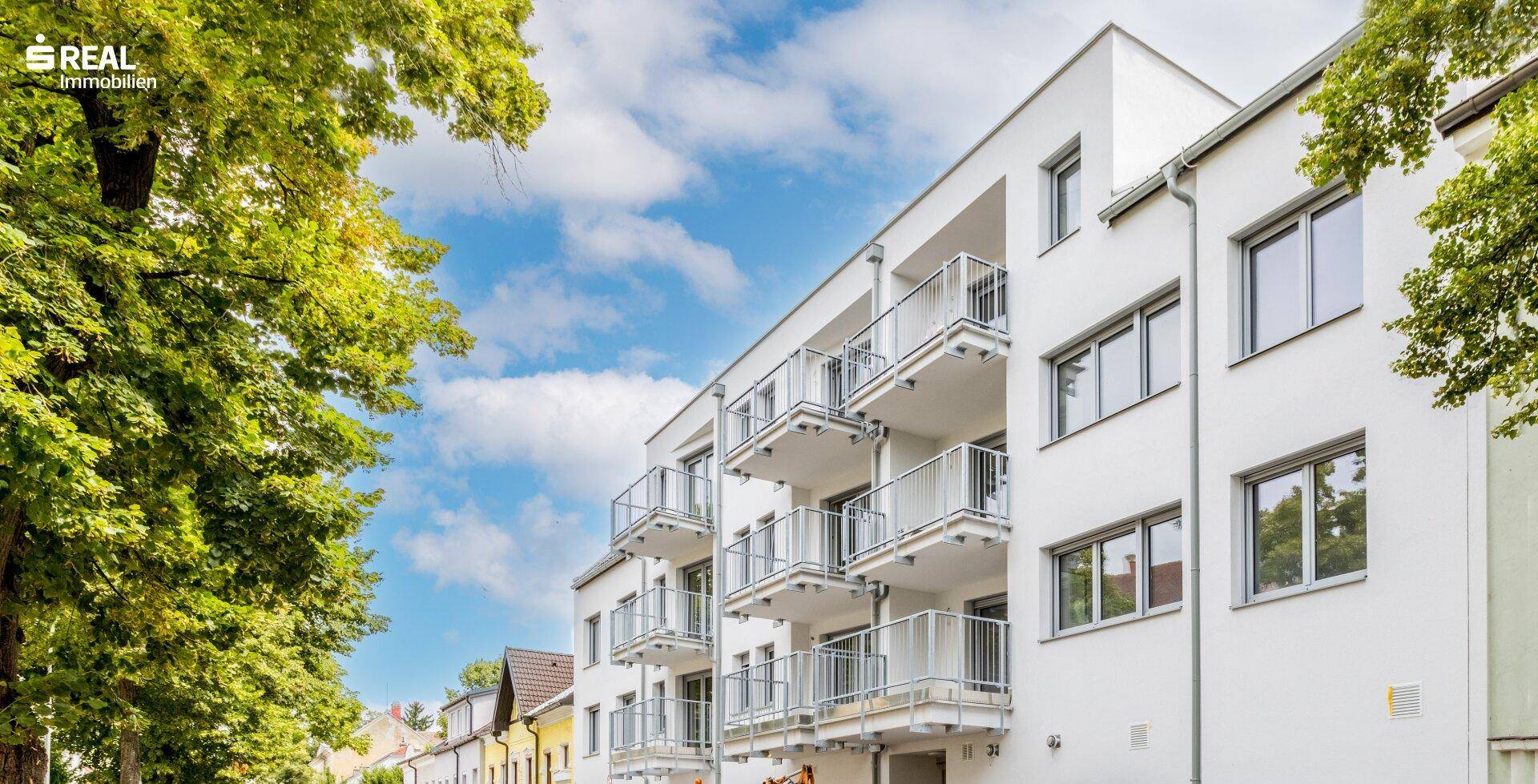 Modernes Mehrfamilienhaus mit weißer Fassade und zahlreichen Balkonen unter blauem Himmel.