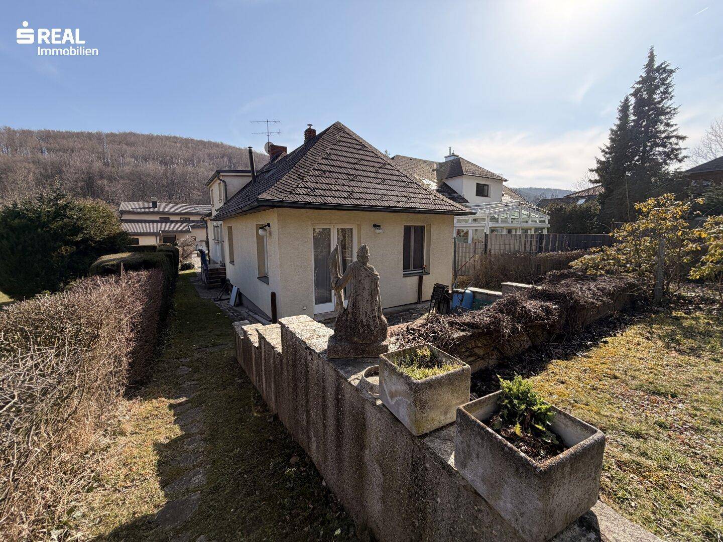 Gartenbereich hinter dem Haus mit Steinmauer, Rasenfläche und Blick auf die Umgebung.