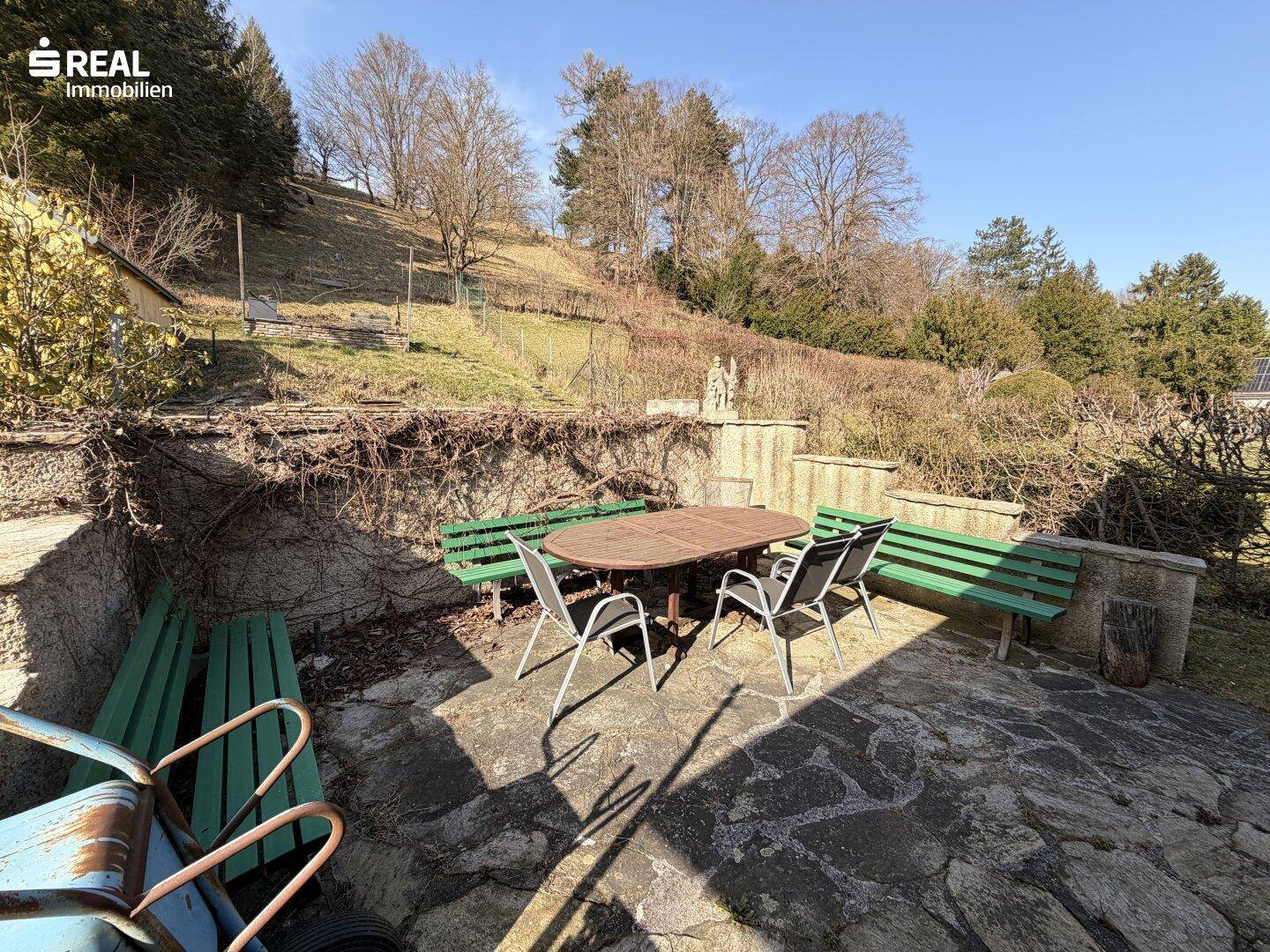 Gemütlicher Außenbereich mit Steinfliesen, Gartentisch und Bänken, ideal zum Entspannen.