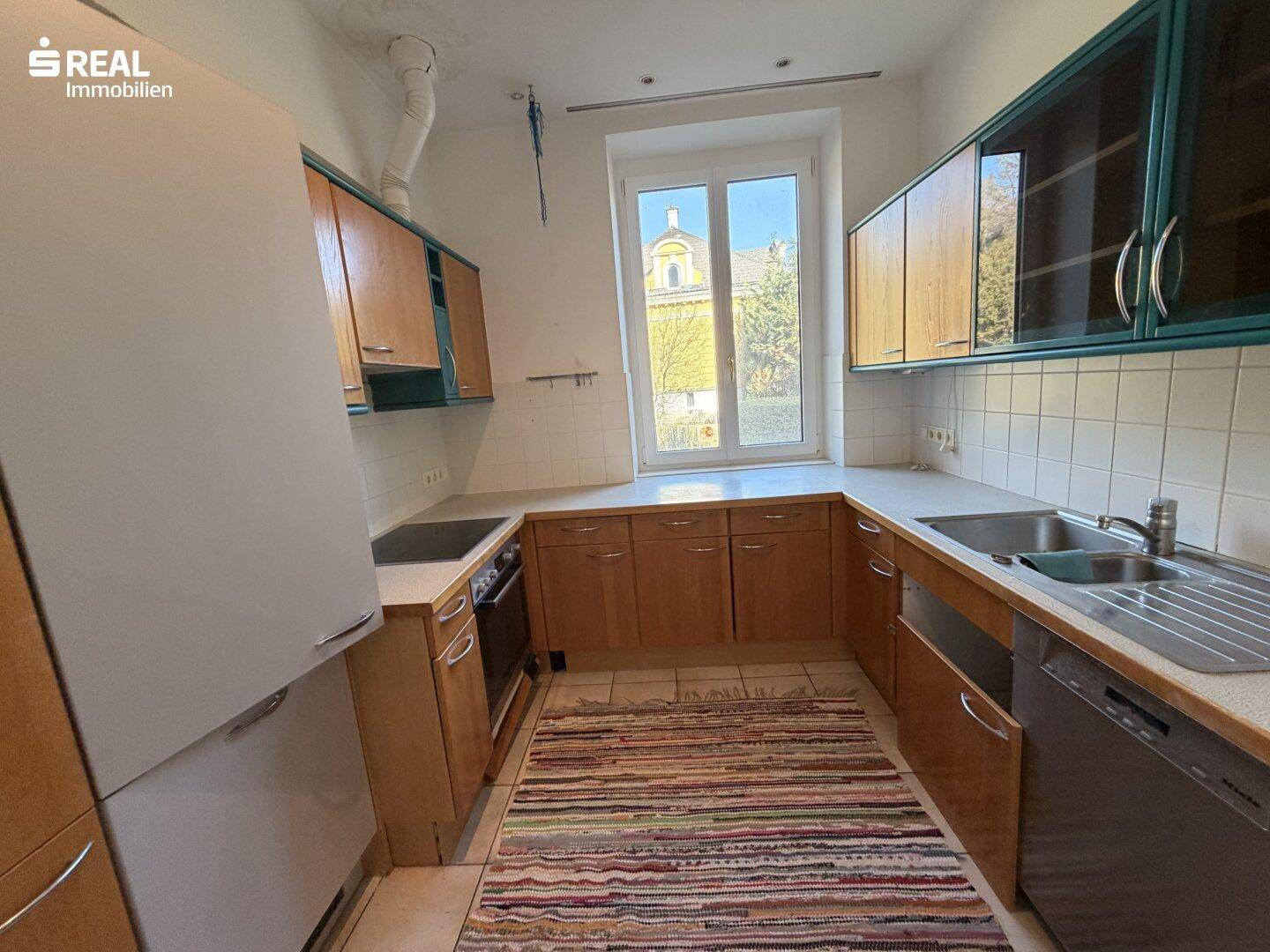 Funktionale Küche mit Holzschränken, hellen Arbeitsplatten und Fenster mit Ausblick.