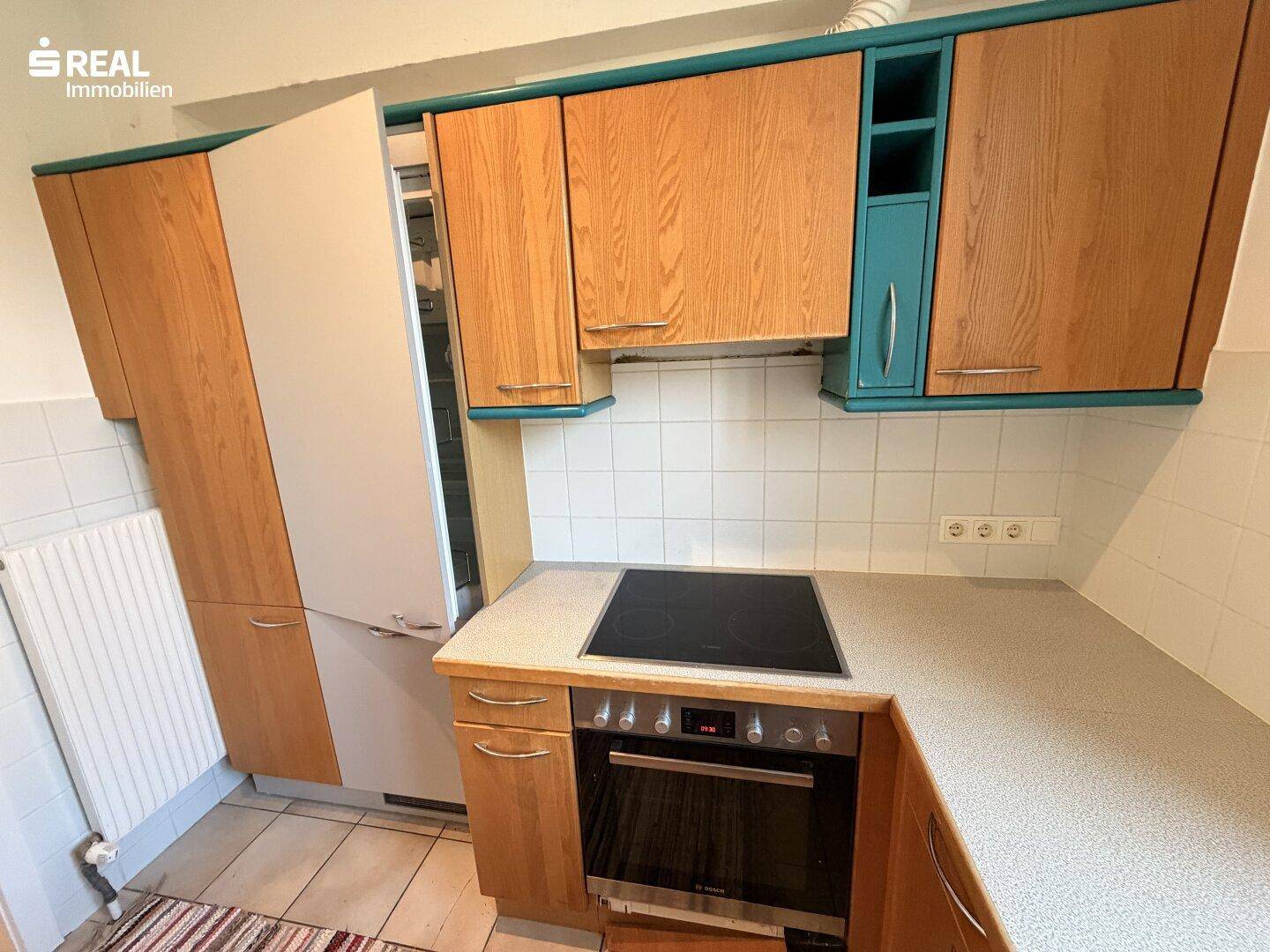 Detailansicht der Küche mit Einbaugeräten, Holzfronten und hellen Fliesen an der Wand.