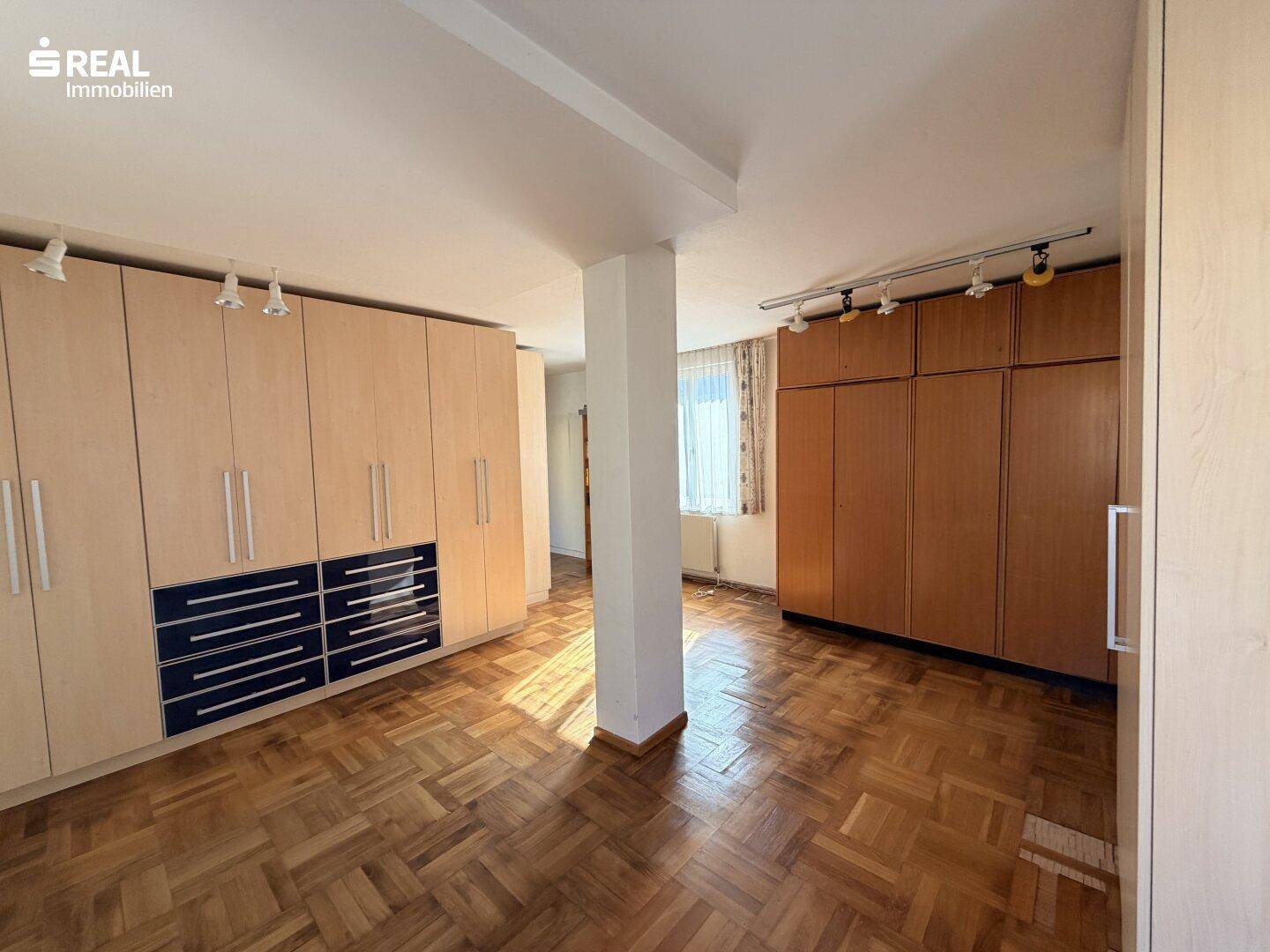 Geräumiges Schlafzimmer mit Fischgrätparkett und umfangreichen Einbauschränken.