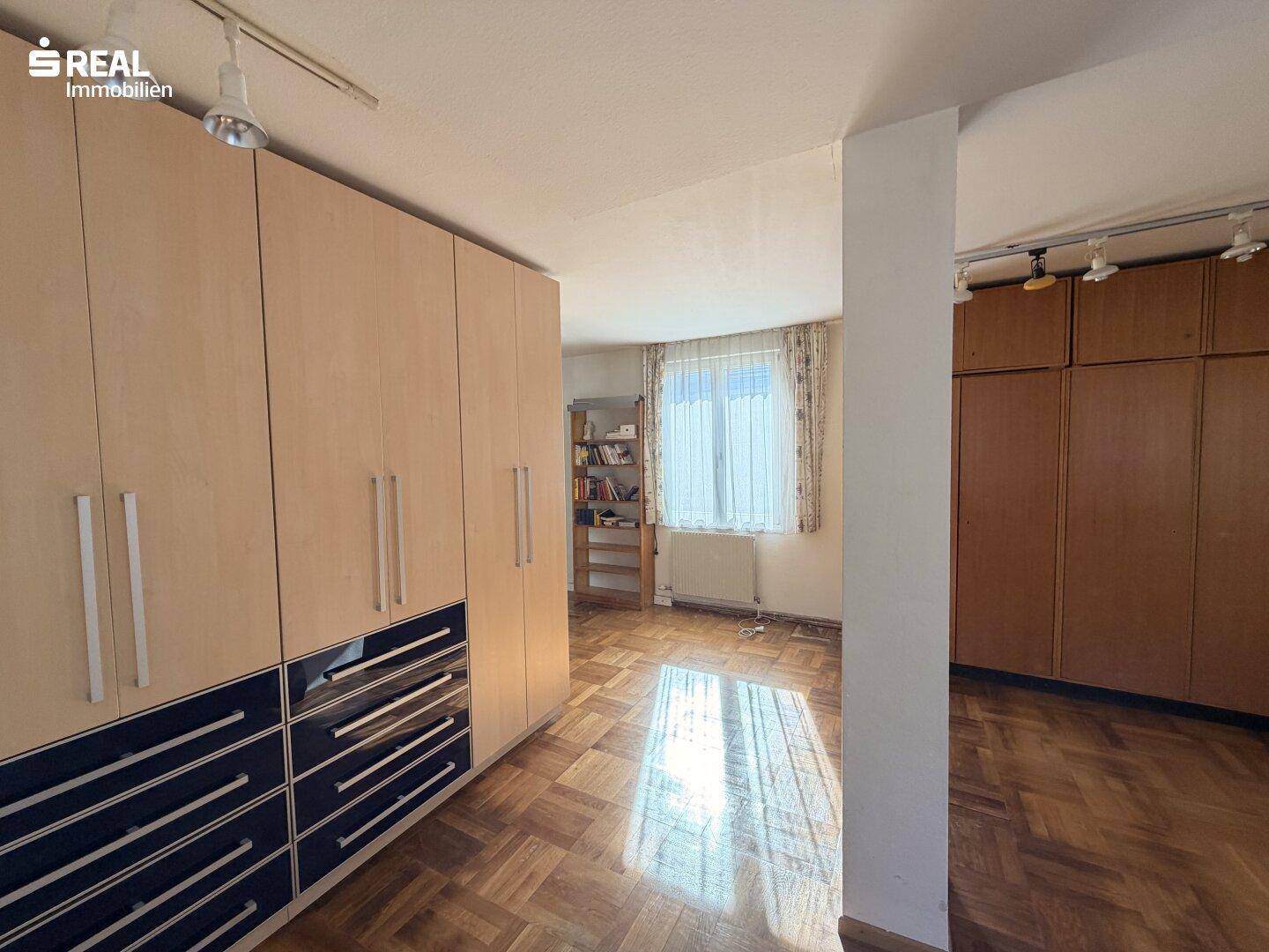 Schlafzimmer mit Einbauschränken, Fischgrätparkett und Fenster mit Blick ins Grüne.