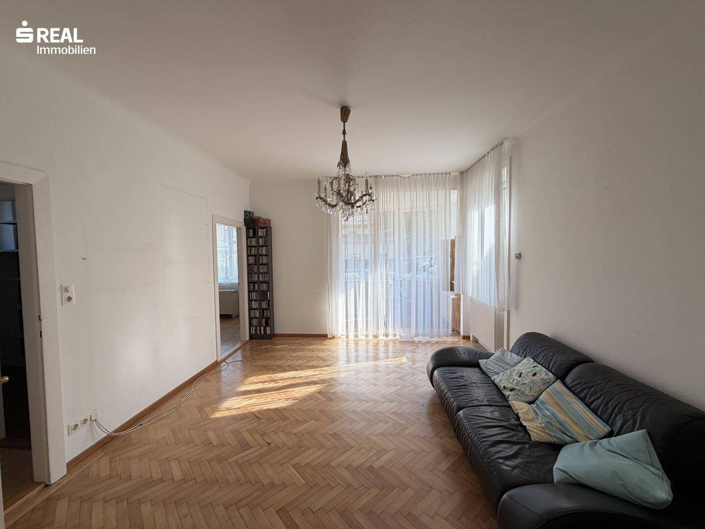 Helles Wohnzimmer mit Fischgrätparkett, Ledersofa und Kronleuchter.