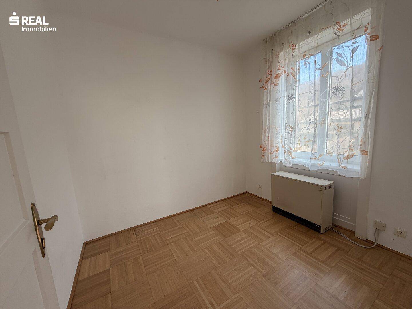 Kleines Zimmer mit Fischgrätparkett, Fenster und Heizkörper, ideal als Gästezimmer.