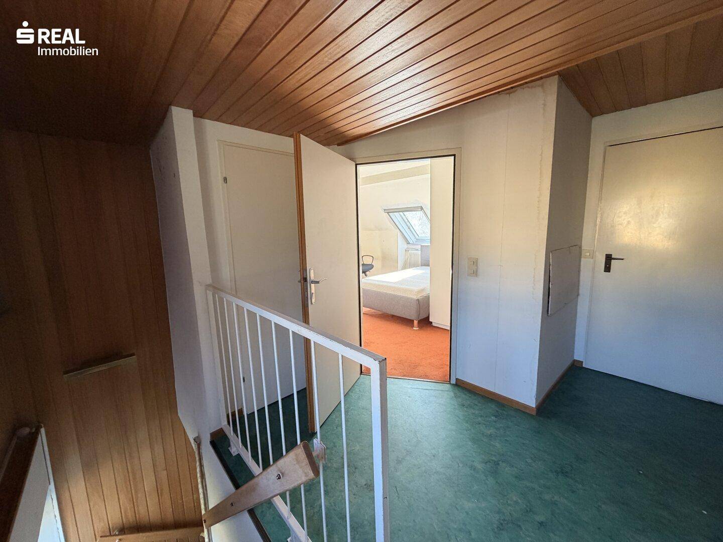 Flurbereich mit Holzdecke und Treppe zum Dachgeschoss, mit Blick in ein Zimmer.