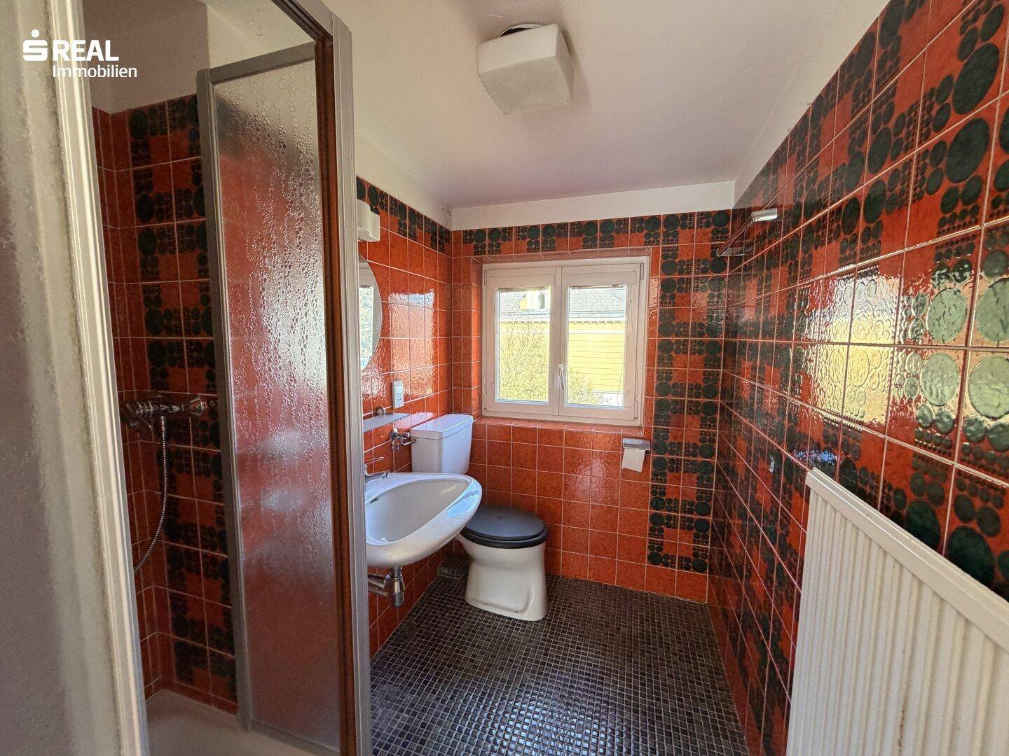 Badezimmer im Dachgeschoss mit Duschkabine, WC und farbigen Fliesen im 80er-Jahre-Stil.