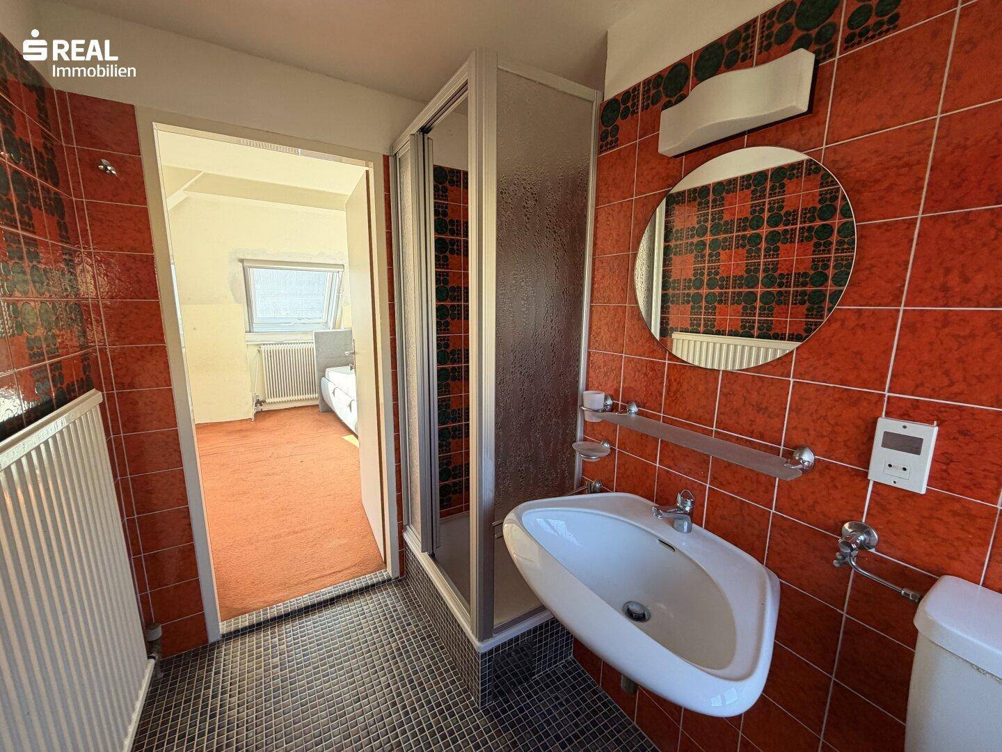 Badezimmer im Dachgeschoss mit Duschkabine, Waschbecken und farbigen Fliesen.
