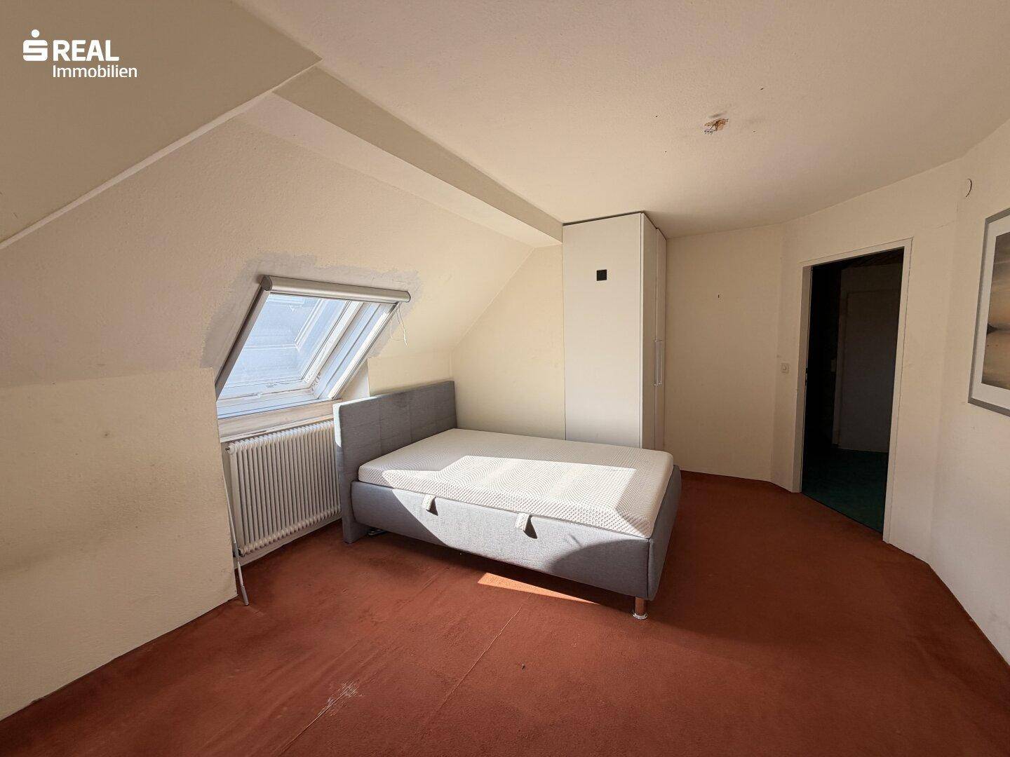 Schlafzimmer im Dachgeschoss mit Dachschräge, Dachfenster und Teppichboden.
