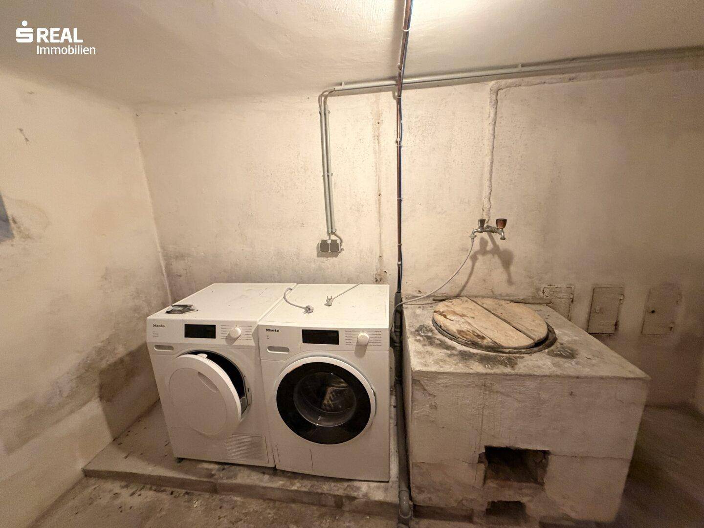 Waschküche im Keller mit Waschmaschine, Trockner und altem Waschtrog.
