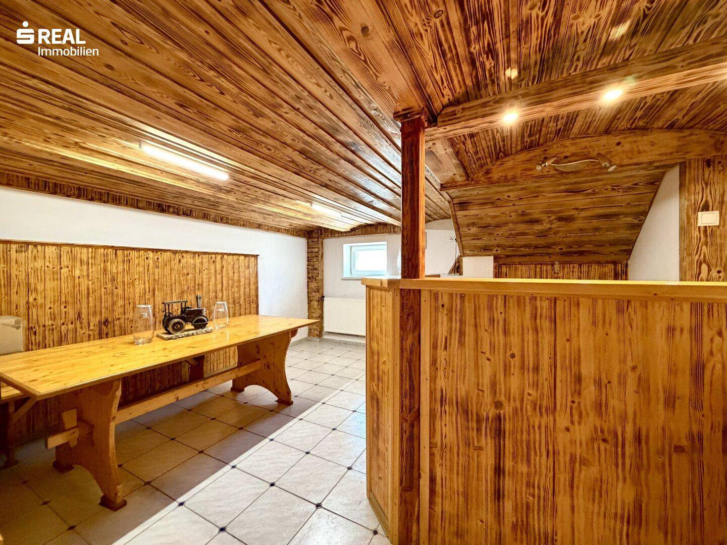 Rustikaler Kellerraum mit Holztisch, Bänken und Holzverkleidung an Wänden und Decke.