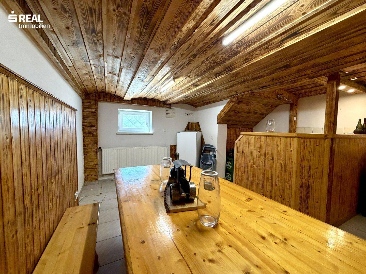 Rustikaler Kellerraum mit Holztisch, Bänken und Holzverkleidung an Wänden und Decke.