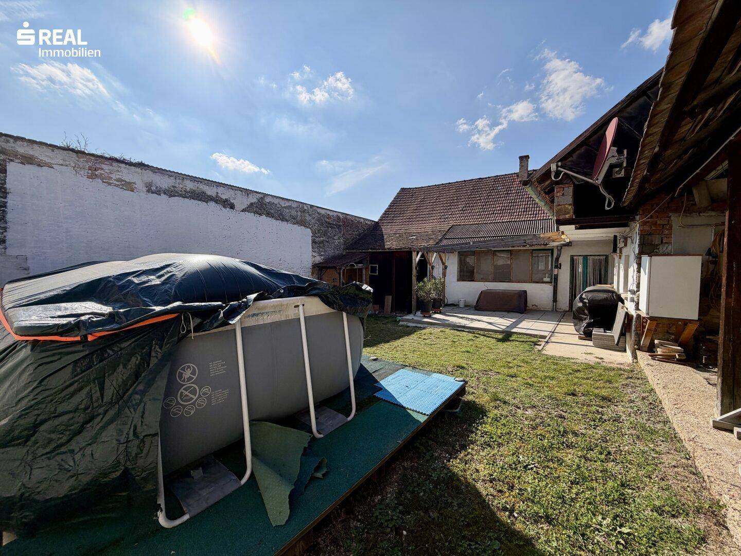 Gartenbereich mit Rasenfläche und einem abgedeckten Aufstellpool unter blauem Himmel.