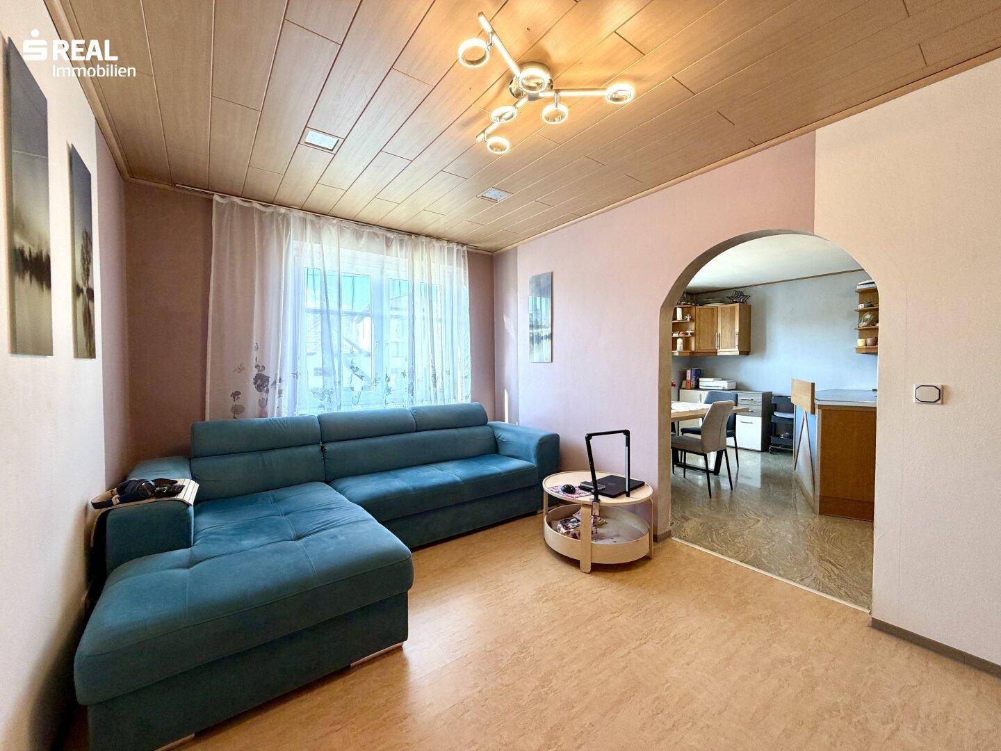 Helles Wohnzimmer mit Ecksofa, Holzdecke und offenem Übergang zum Essbereich.