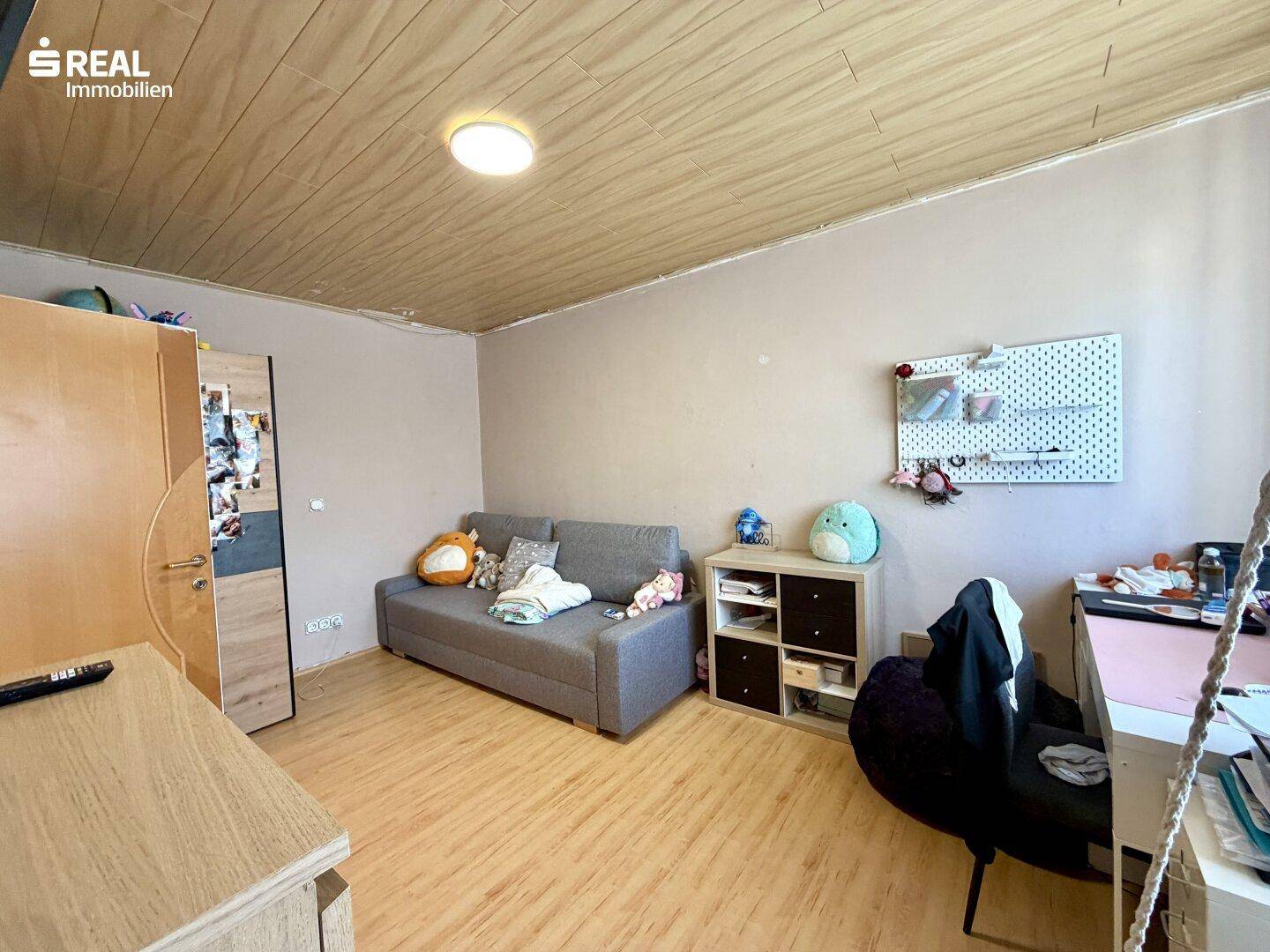Helles Zimmer mit Schlafsofa, Holzdecke und Stauraum.