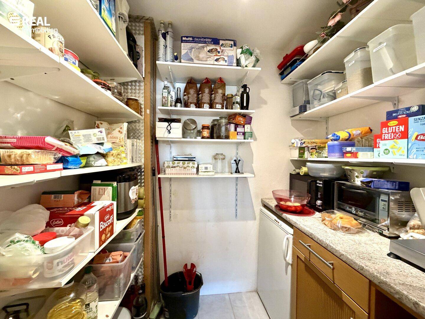 Gut organisierte Speisekammer mit Regalen voller Vorräte und einem kleinen Kühlschrank.