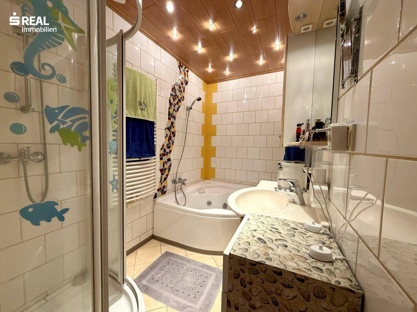Badezimmer mit Eckbadewanne, Duschkabine und Holzdecke.