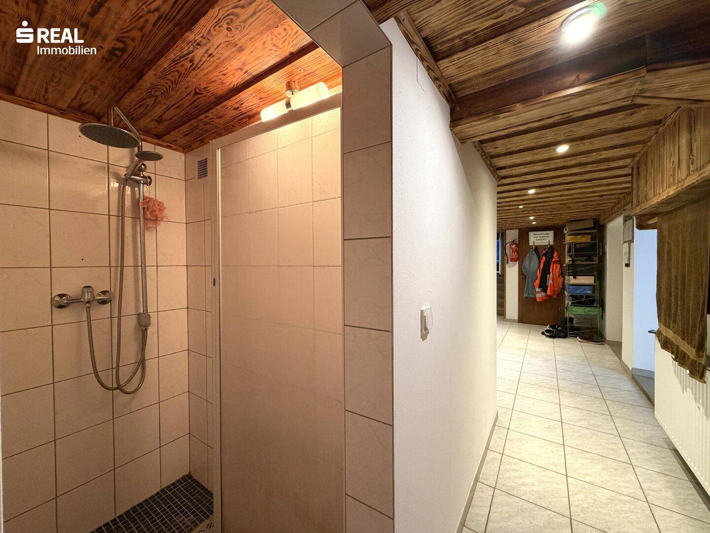 Duschbereich im Keller mit Fliesenwänden und Holzdecke.