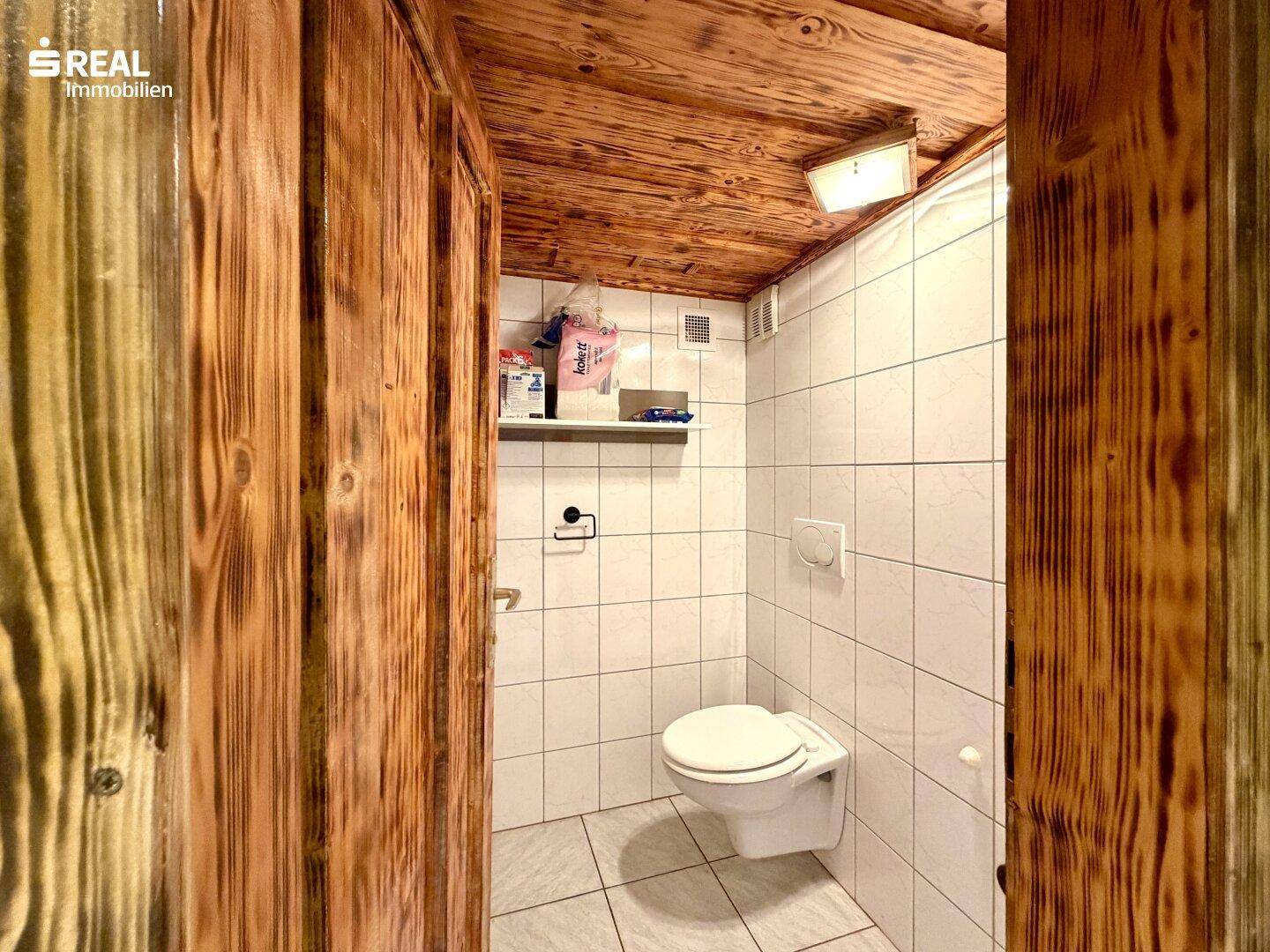 Separate Toilette im Keller mit Fliesenwänden und Holzdecke.