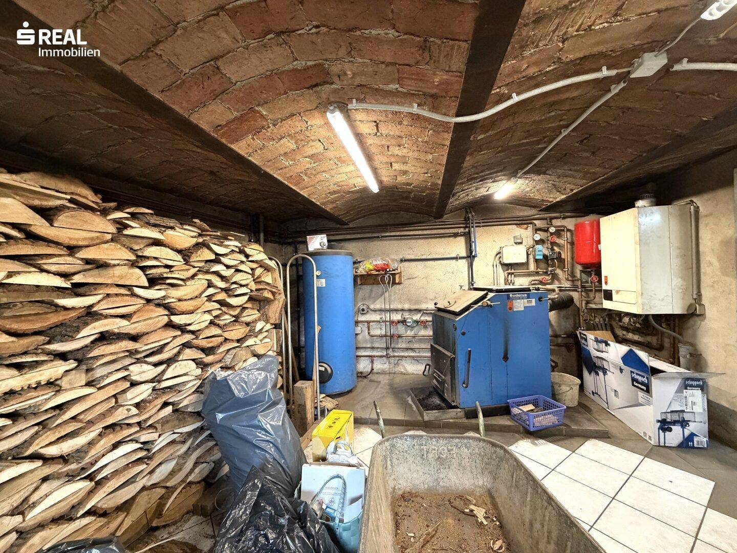Heizraum im Keller mit Holzstapel, Heizkessel und Warmwasserspeicher.