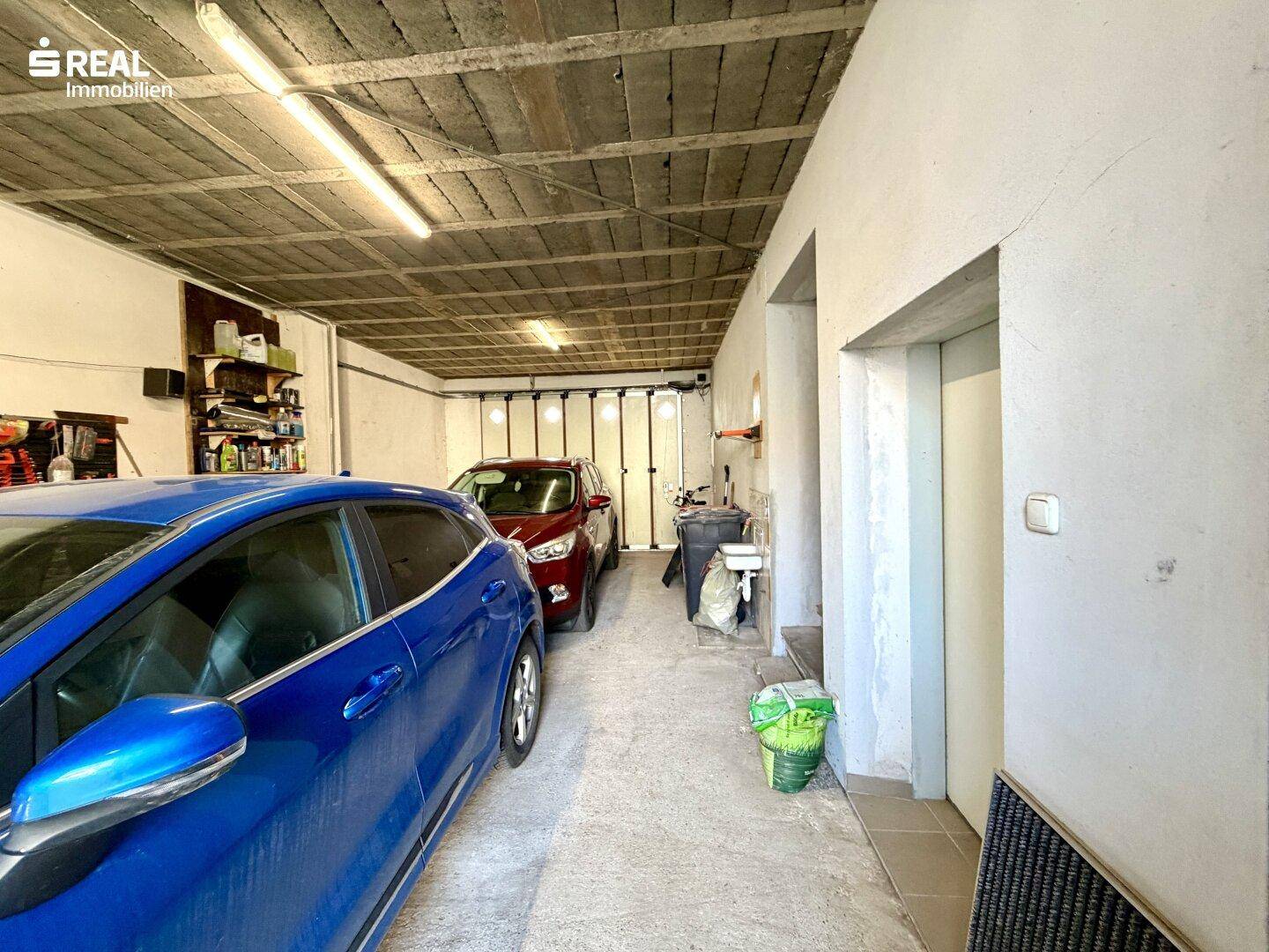 Geräumige Doppelgarage mit zwei geparkten Autos und Stauraum.