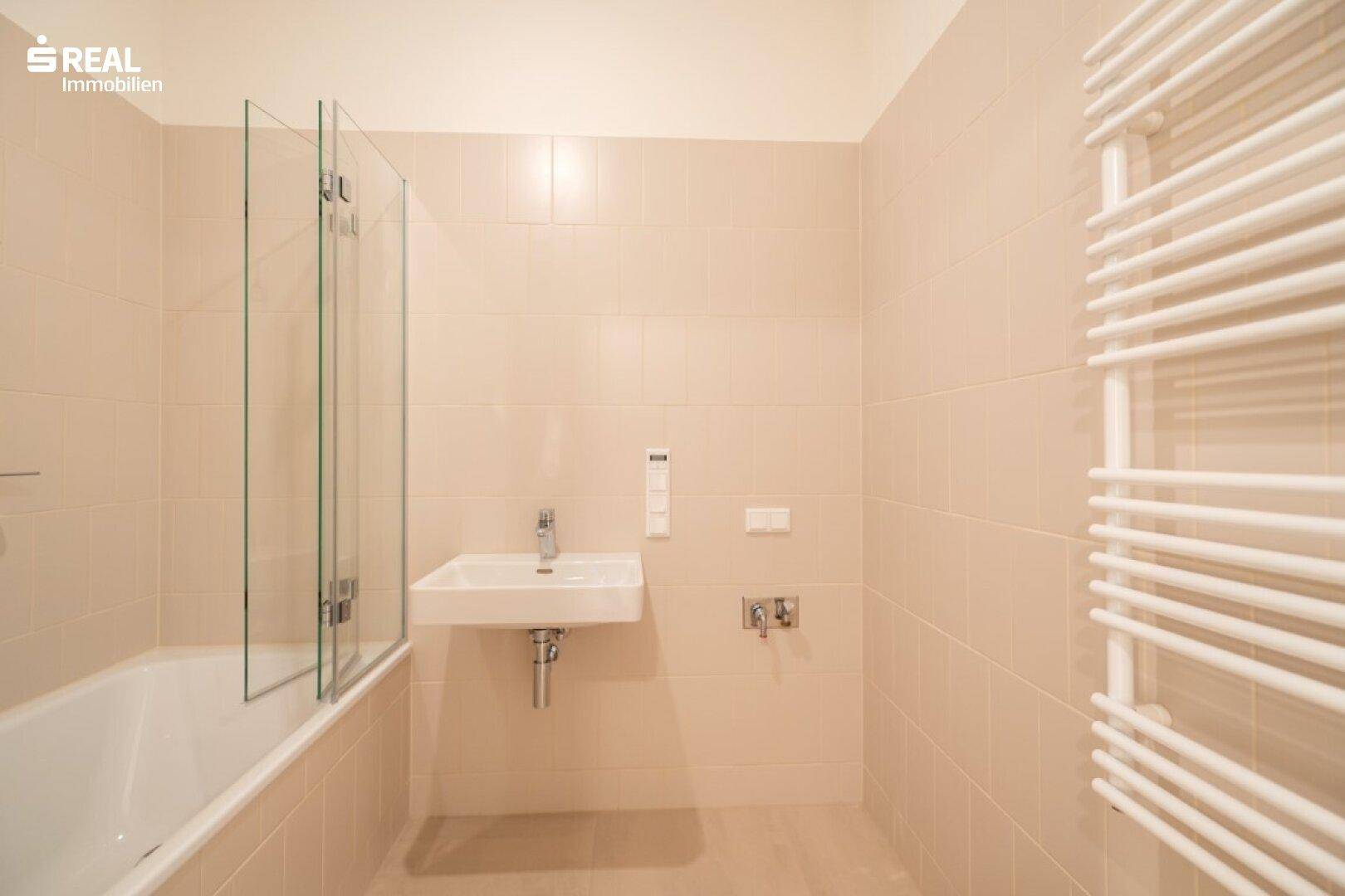 Modernes Badezimmer mit Badewanne, Duschwand und beheiztem Handtuchhalter.