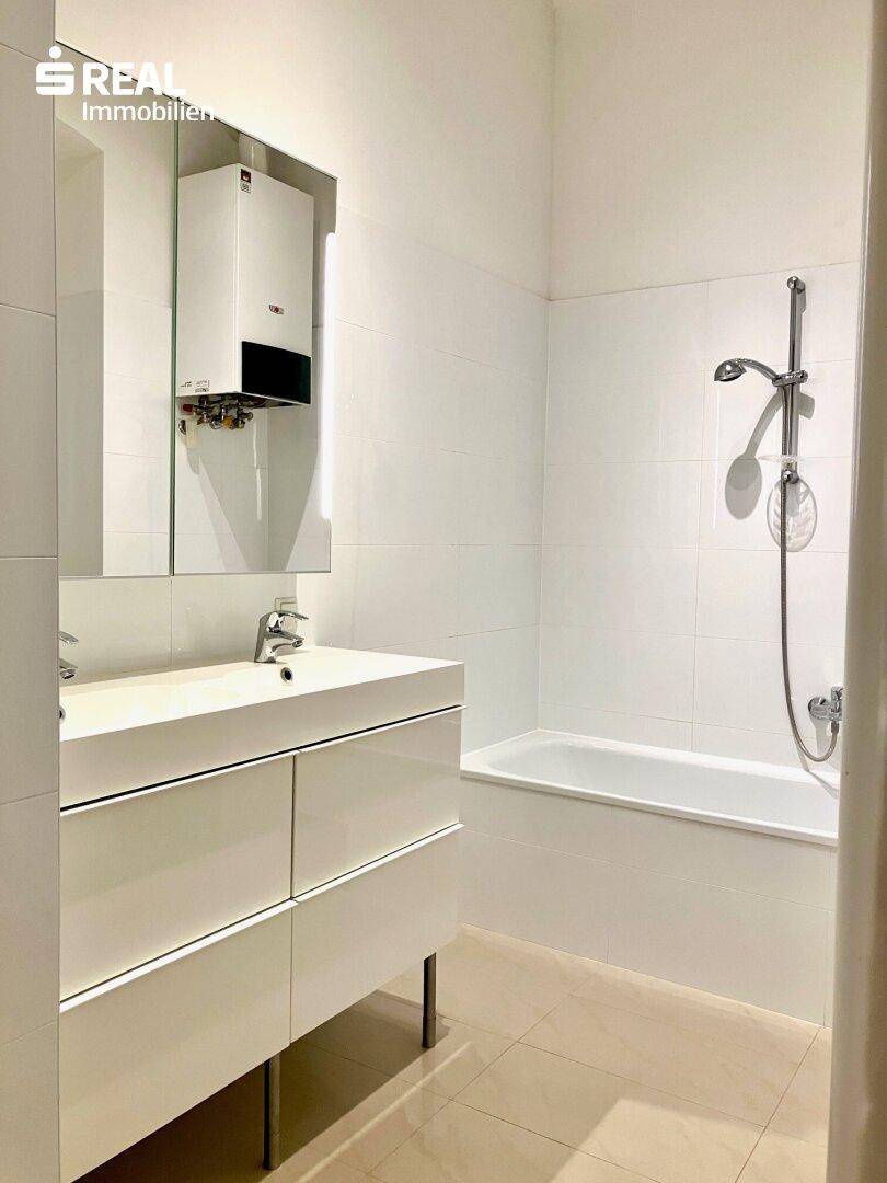 Modernes Badezimmer mit weißen Fliesen, Doppelwaschbecken und Badewanne mit Duschfunktion.