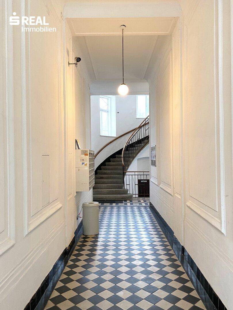 Langer Eingangsbereich mit auffälligem Schachbrettmuster-Fliesenboden, der zum Treppenhaus führt.