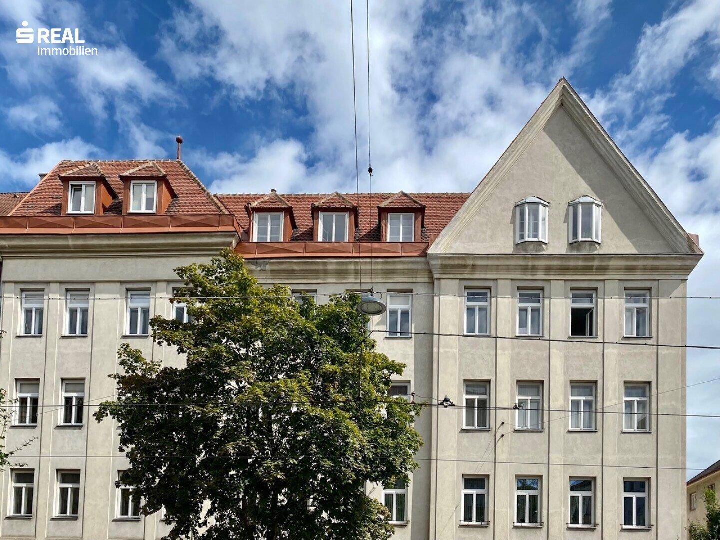 Historisches Gebäude mit klassischer Fassade, vielen Fenstern und Mansarddächern unter blauem Himmel.