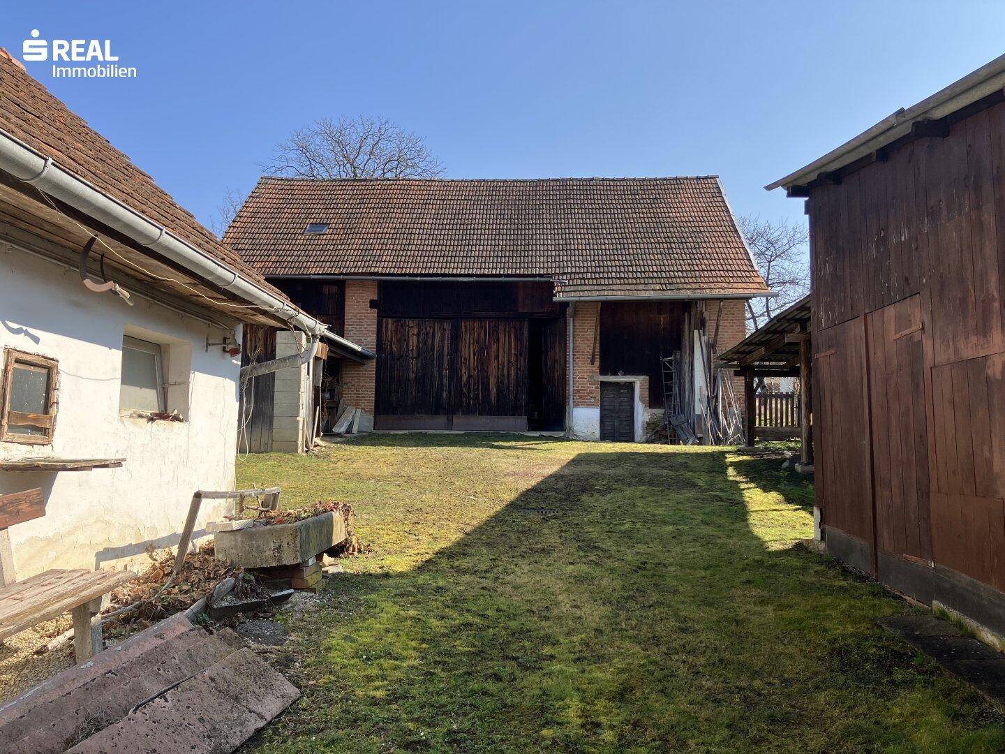 Großes Scheunengebäude mit Holztoren und einem weitläufigen Hofbereich mit Rasen, ideal für Landwirtschaft.