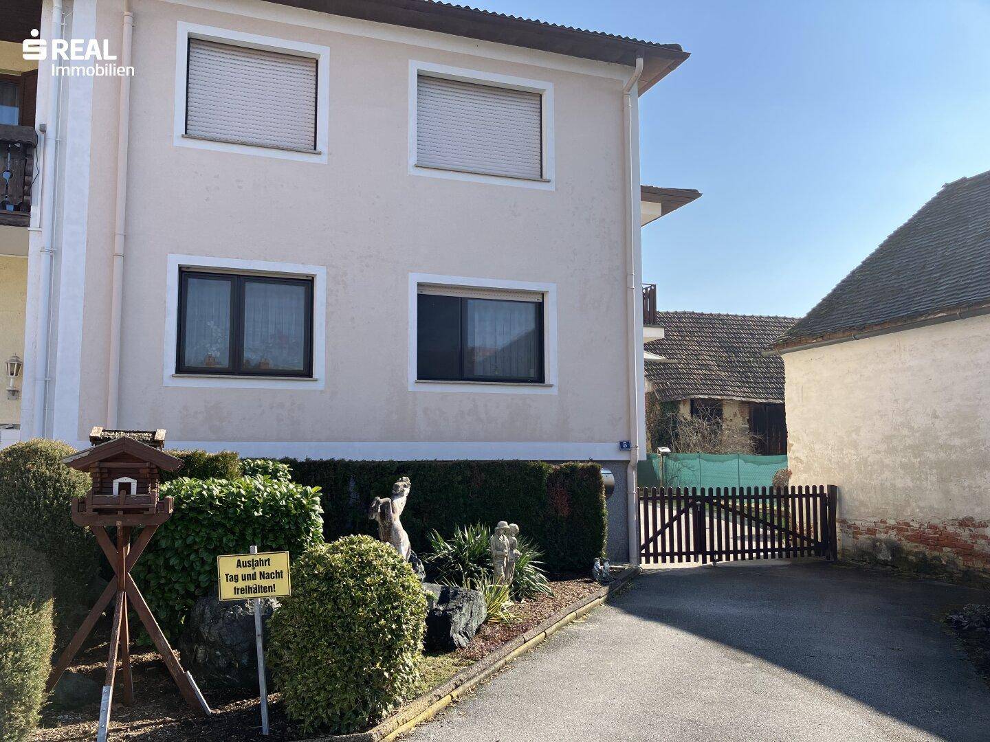 Vorderansicht eines Wohnhauses mit beiger Fassade, Rollläden und einem gepflegten Vorgarten.