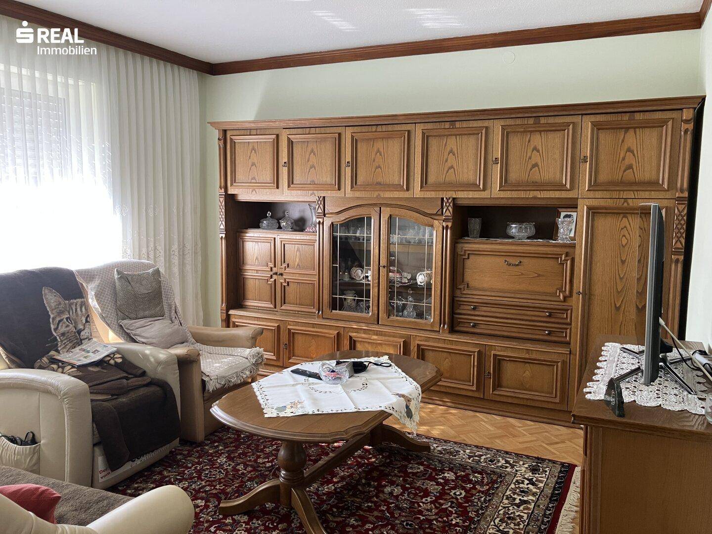 Wohnzimmer mit großer Holzschrankwand, Teppichboden und traditioneller Einrichtung, bietet viel Platz.