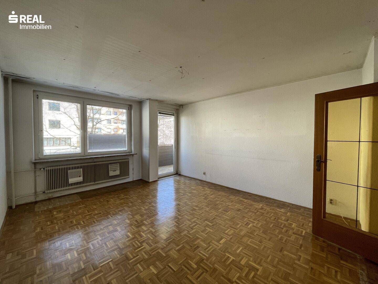 Helles Wohnzimmer mit Fischgrätparkettboden und Zugang zu einem Balkon.