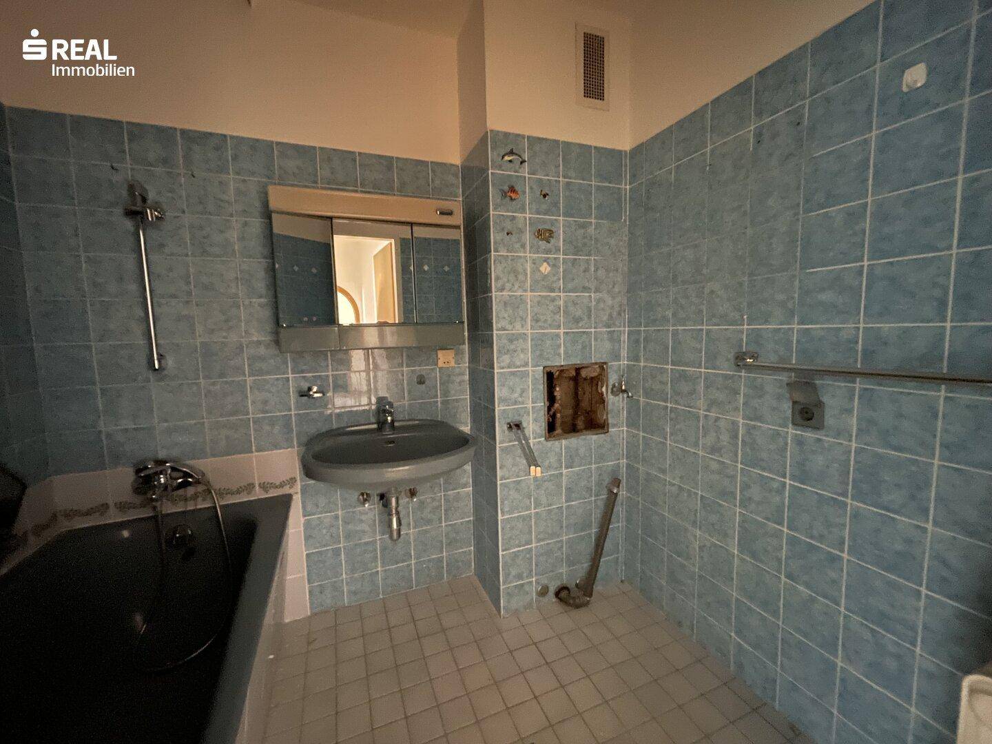 Badezimmer mit blauen Fliesen, Badewanne und Waschbecken, das eine Modernisierung benötigt.