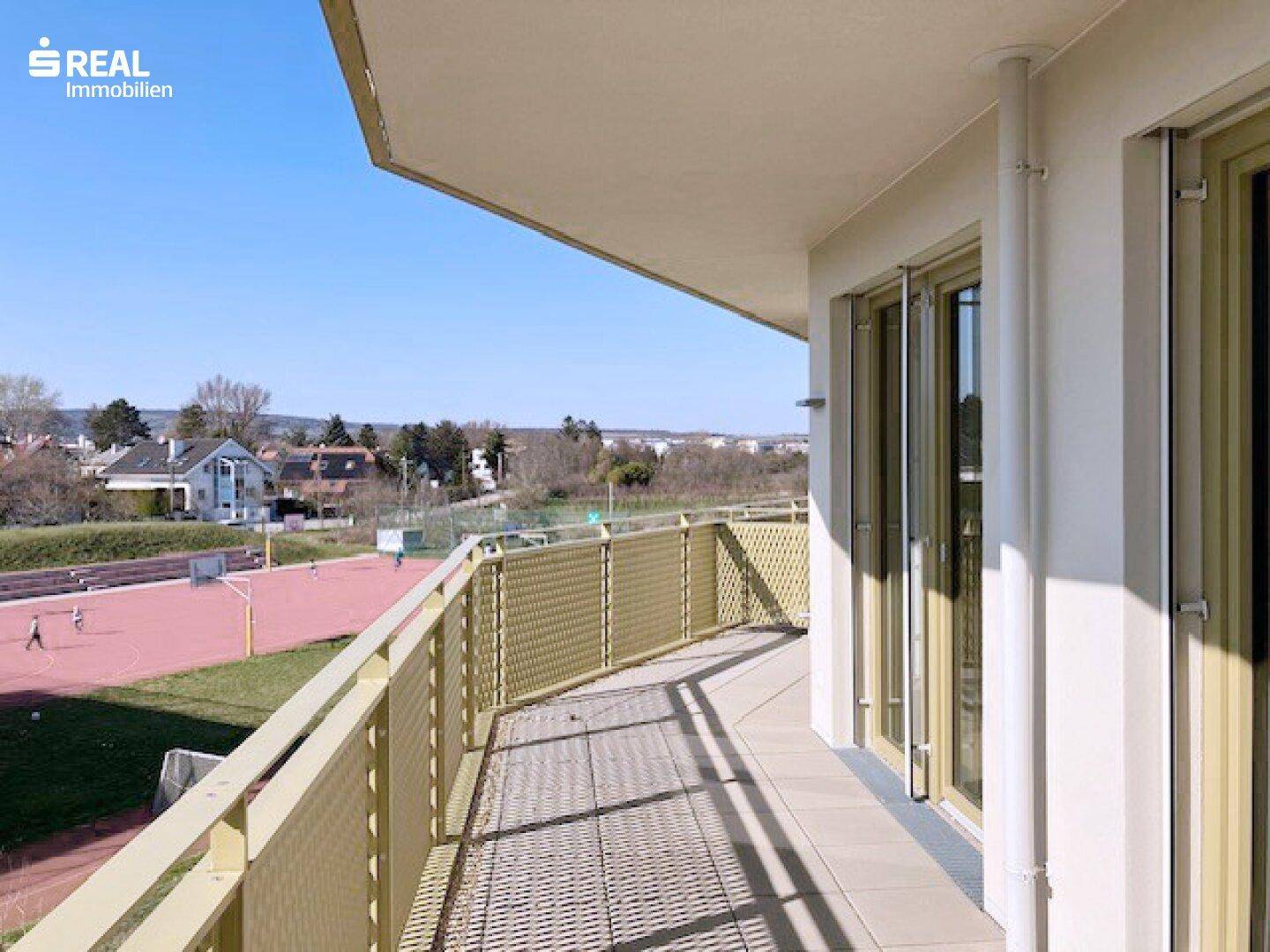 Geräumiger Balkon mit Fliesenboden und weitem Blick über Sportanlagen und die Umgebung.
