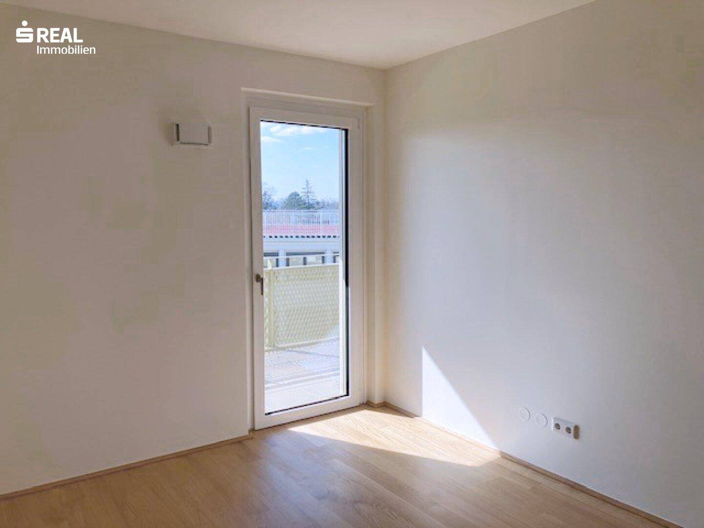 Helles Schlafzimmer mit Parkettboden und Zugang zu einem Außenbereich, gut belichtet.