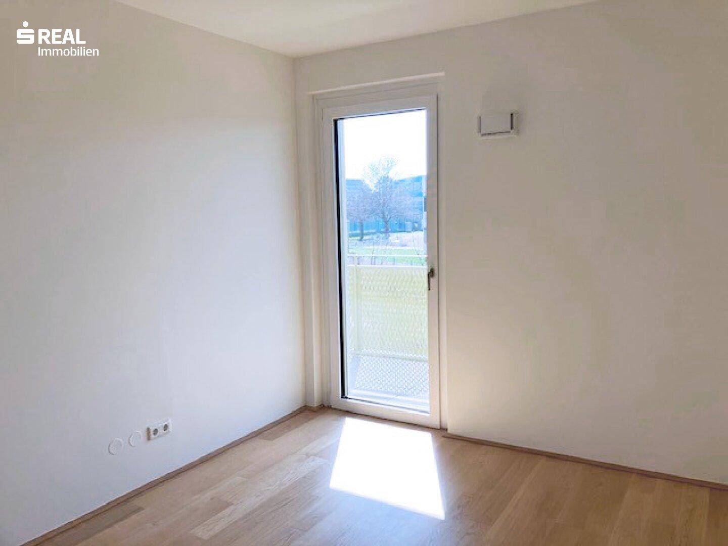 Helles Zimmer mit Parkettboden und Zugang zu einem kleinen Außenbereich.