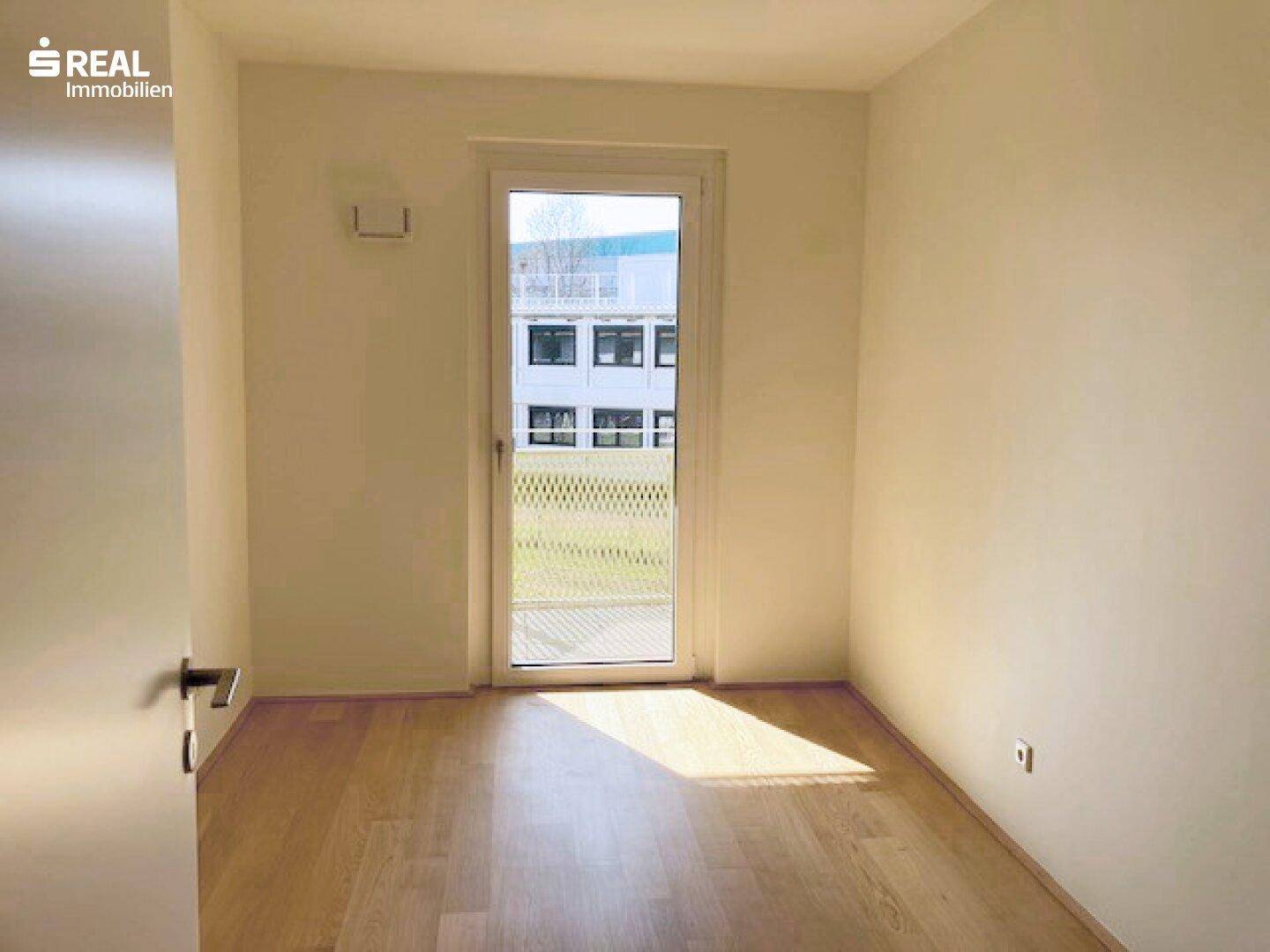 Kleines, helles Zimmer mit Parkettboden und Fenster mit Blick ins Grüne.