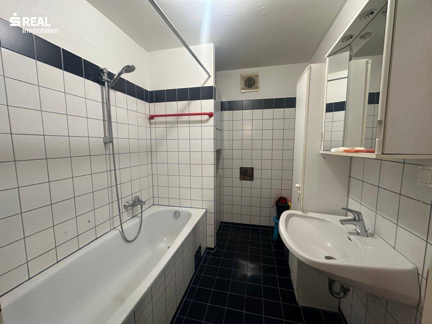 Badezimmer im 80er-Jahre-Stil mit Badewanne, Waschbecken und schwarz-weißen Fliesen.