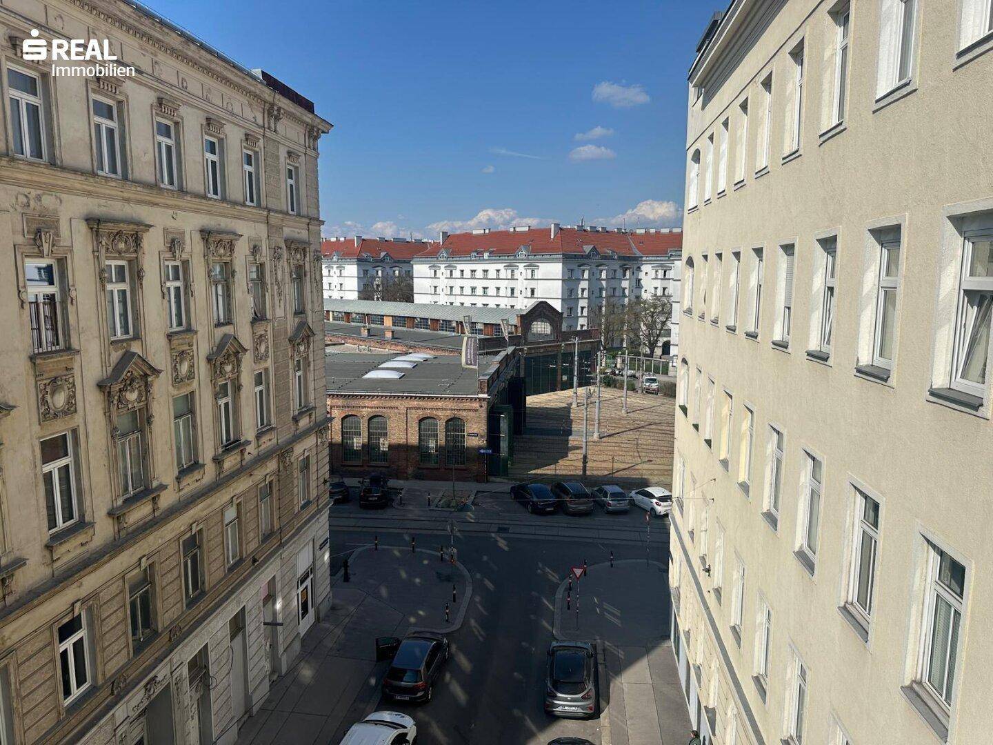 Blick auf die belebte Stadtstraße mit parkenden Autos und umliegenden Gebäuden.