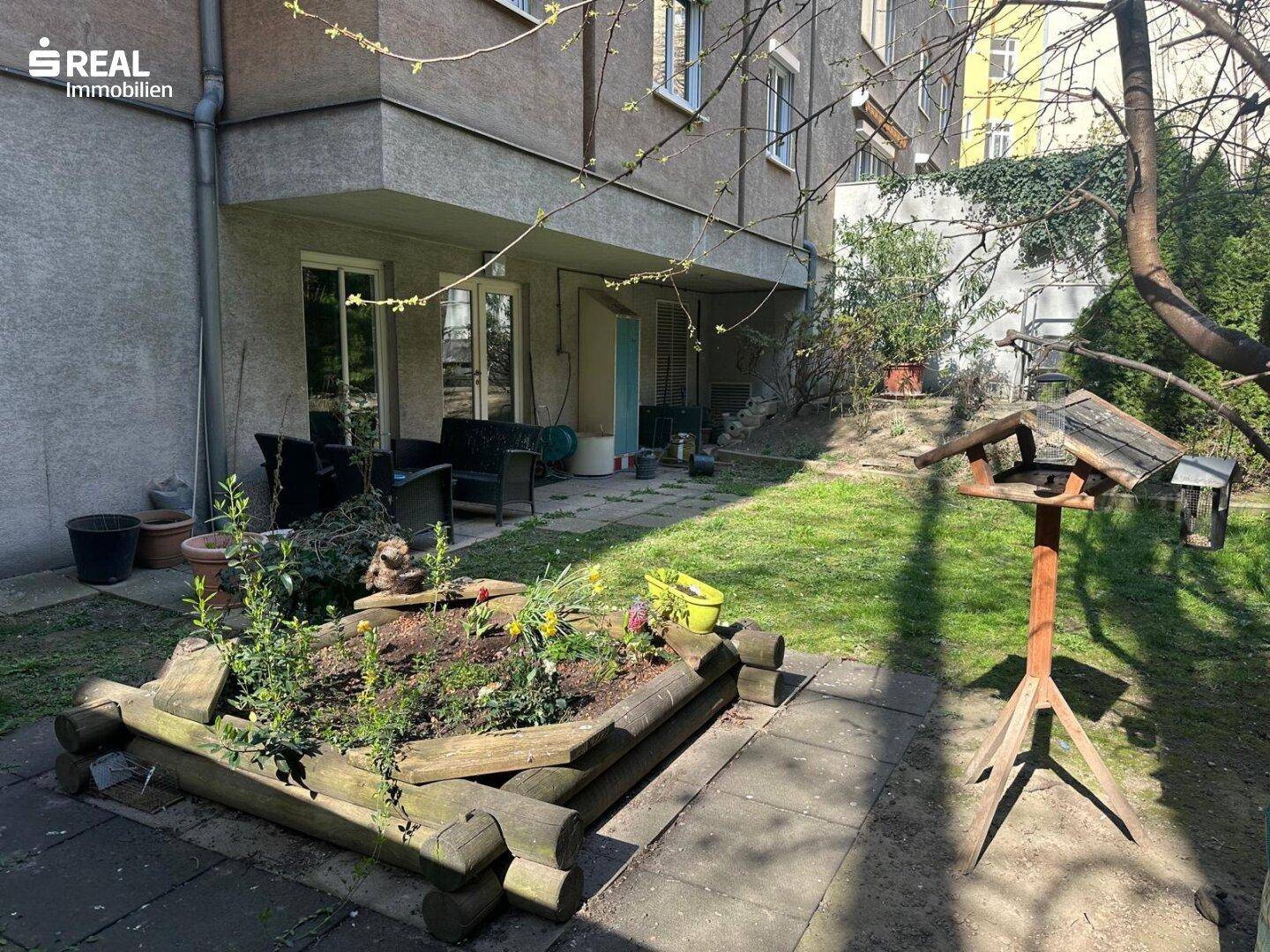 Sonniger Gartenbereich mit Rasenfläche, Hochbeet und Sitzgelegenheiten im Freien.