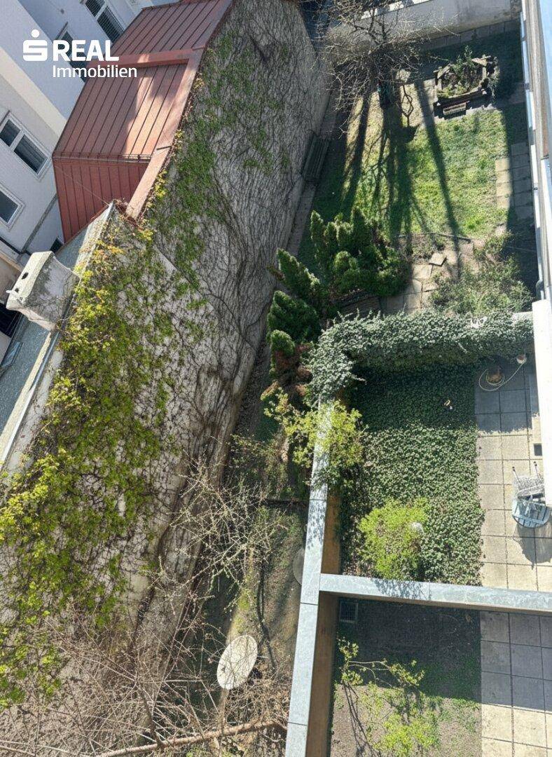 Blick von oben auf einen begrünten Innenhof mit verschiedenen Pflanzen und Sitzbereichen.