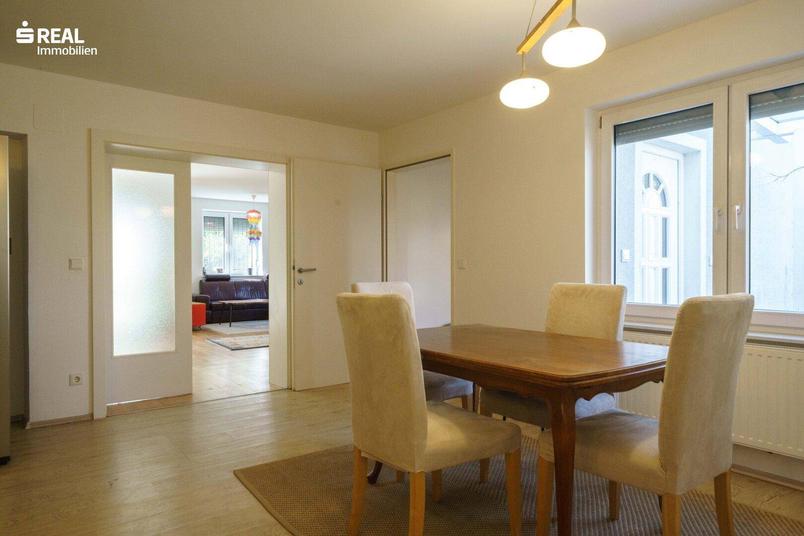 Essbereich mit Holztisch und bequemen Stühlen, angrenzend an einen weiteren Wohnraum.