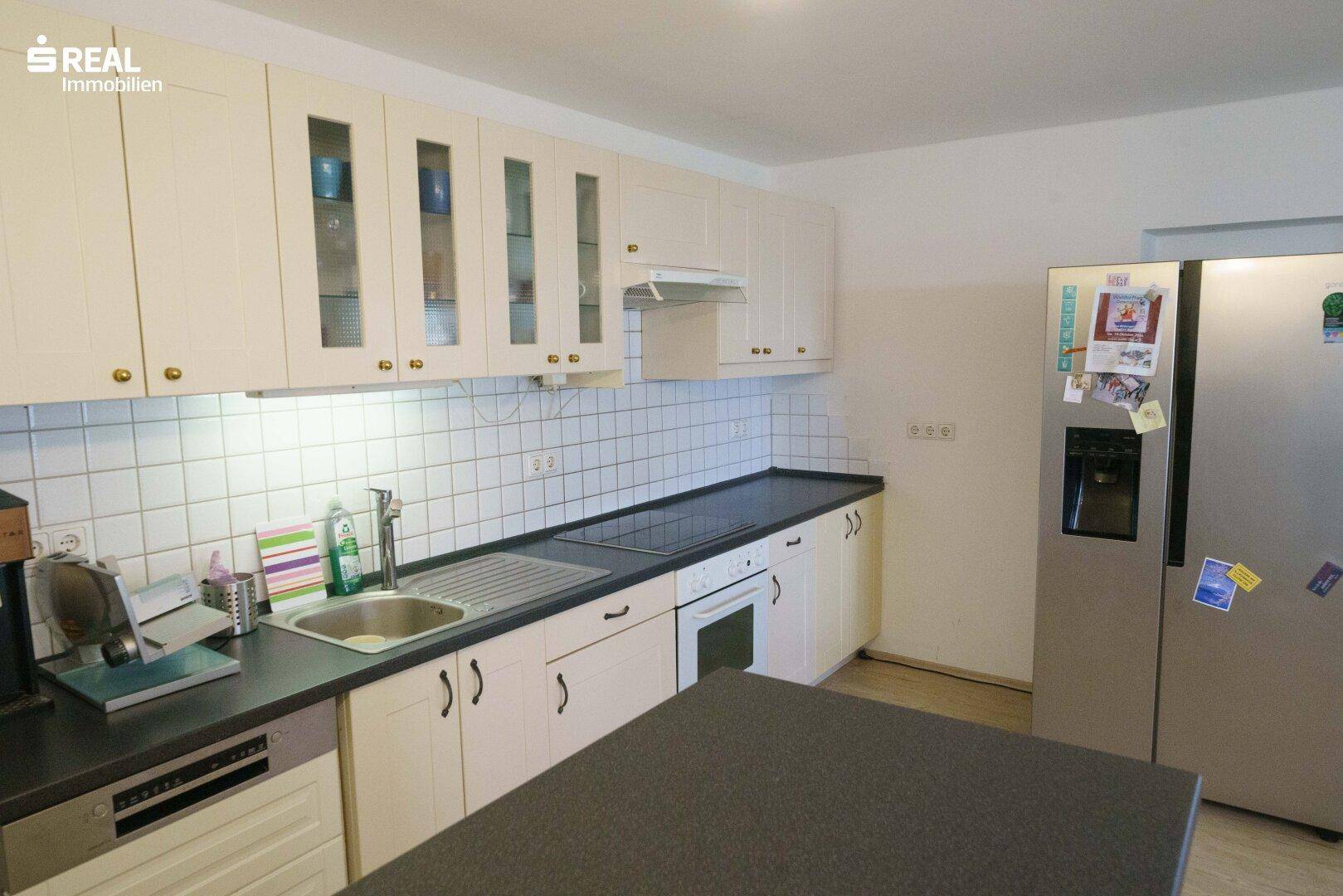 Gut ausgestattete Küche mit weißen Schränken, Fliesenrückwand und großem Kühlschrank.