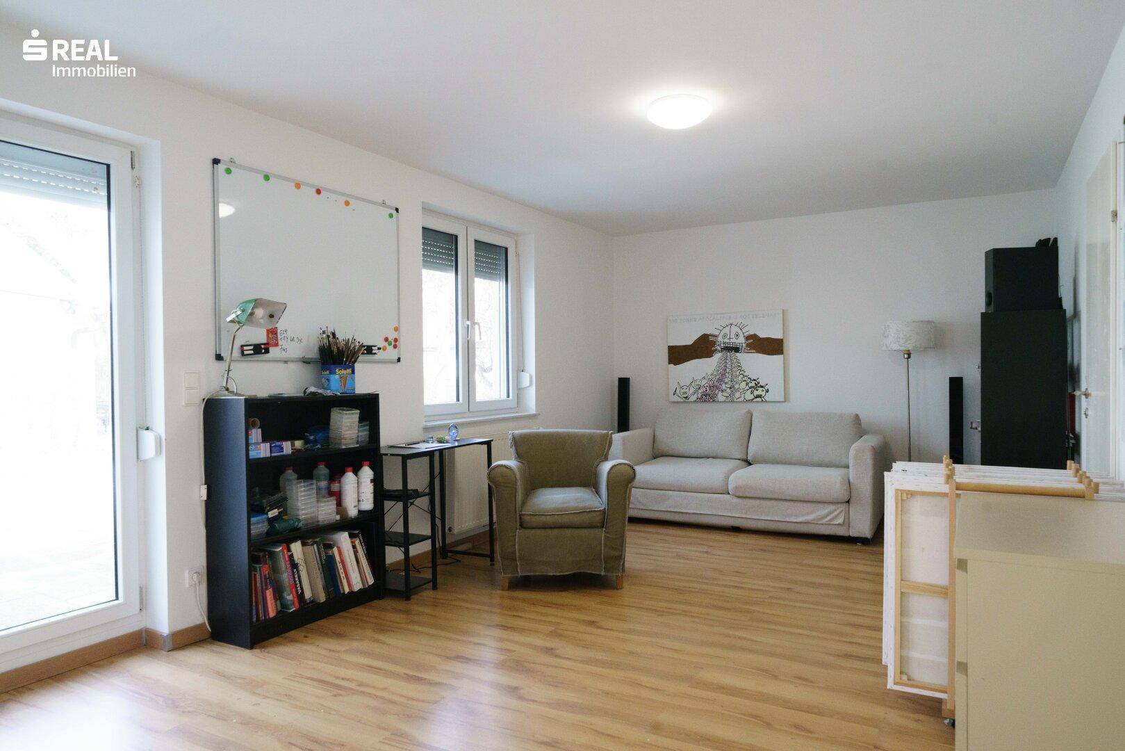 Heller Wohnraum mit Laminatboden, Sofa, Sessel und Zugang zum Außenbereich.