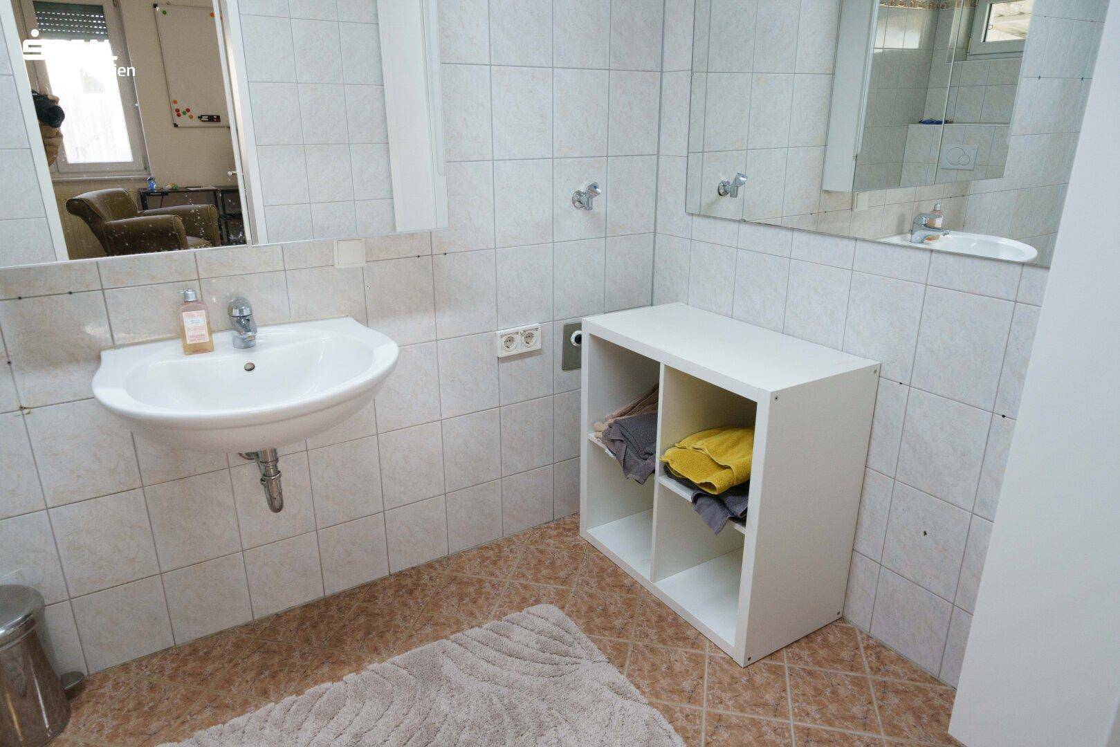 Badezimmer mit Waschbecken, großem Spiegel und hellen Fliesen an den Wänden.