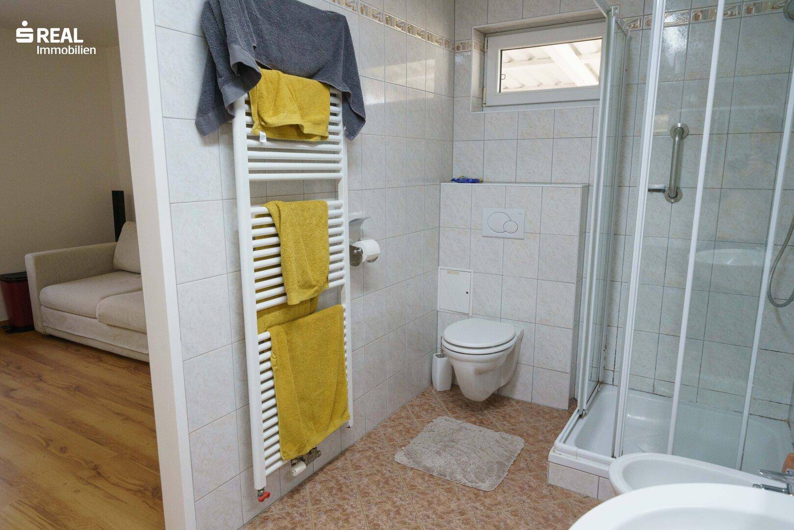Badezimmer mit Duschkabine, WC und beheiztem Handtuchhalter, hell gefliest.