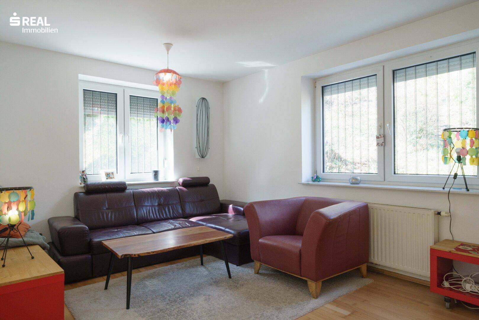 Heller Wohnbereich mit bequemer Couch, bunten Lampen und großen Fenstern.