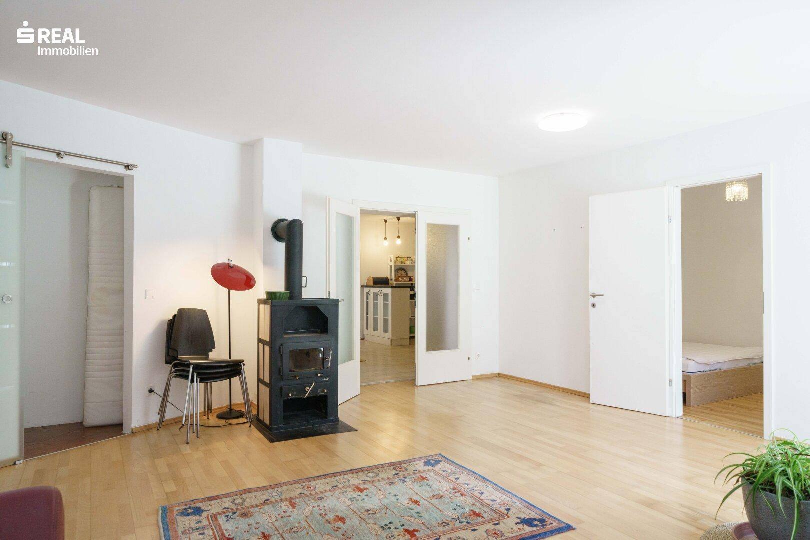 Geräumiges Wohnzimmer mit Kaminofen, Holzboden und Durchgang zu Küche und Schlafzimmer.