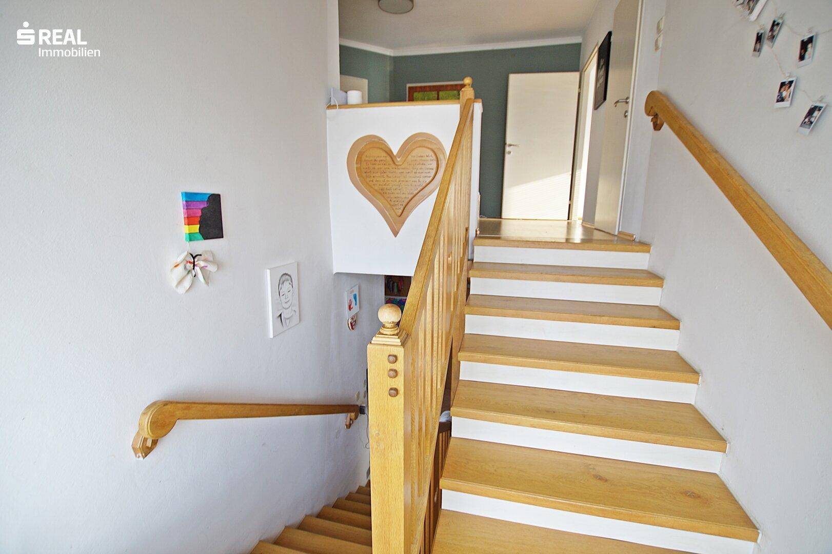 Treppenaufgang mit Holzgeländer und weiß gestrichenen Wänden, führt in die obere Etage.